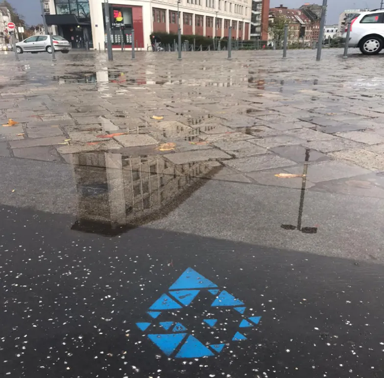 Marquage bleu sur une place mouillée où se reflètent les façades