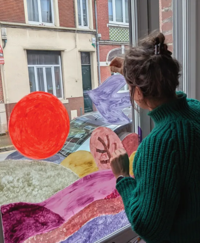 Une artiste peint des formes colorées sur une vitre