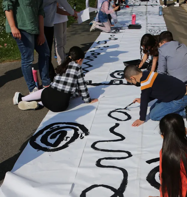 Élèves dessinant des lignes noires sur un long rouleau de papier